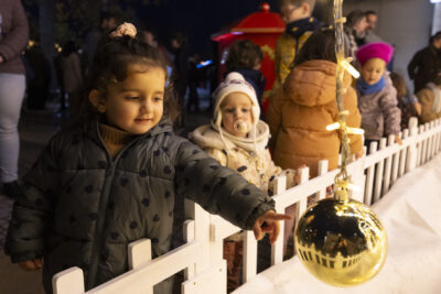 une petite fille tend le doigt vers une boule dorée suspendue par une guirlande lumineuse, un enfant avec une tétine la regarde faire - Agrandir l'image 6 sur 20, fenêtre modale