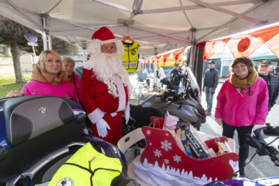 photo du Père Noël derrière le stand des motards au grand cœur, entre deux grosses motos, et avec trois femmes vêtues de rose - Agrandir l'image 8 sur 12, fenêtre modale
