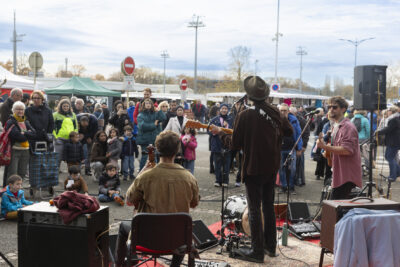 photo d'un concert de trois hommes avec guitare et contrebasse, en extérieur, avec une cinquantaine de personnes arrêtées devant pour écouter - Agrandir l'image 3 sur 12, fenêtre modale