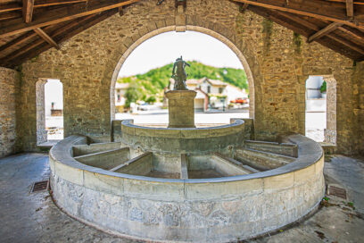 Photo d'un lavoir en pierre sous une sorte de préau en pierre et bois - Agrandir l'image, fenêtre modale