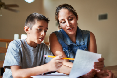 Photo d'une jeune femme qui aide un jeune garçon à faire ses devoirs dans une pièce, il montre une feuille avec un crayon à papier