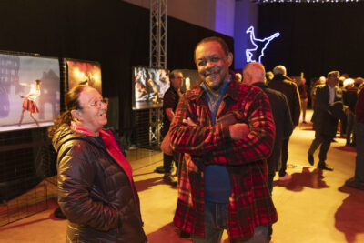 photo d'un homme et d'une femme souriant dans la salle, on voit derrière eux à gauche des grandes photos de spectacles et des personnes rassemblées dans la salle - Agrandir l'image 4 sur 20, fenêtre modale